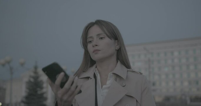 Close up view of annoyed nervous businesswoman in raincoat and suit arguing on phone and then break call. Lady feel disgruntled after bad conversation.