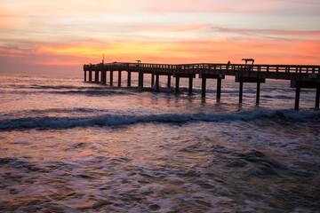 Fototapeta na wymiar Sunrise through a fishing pier at the beach at St Augustine, Florida.