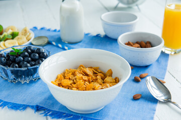 Nutritious healthy breakfast. Bowl with cereals, almonds, blueberry, plant-based milk, and orange fresh juice on a blue napkin and white wooden table. Day diet planning and healthy eating concept.