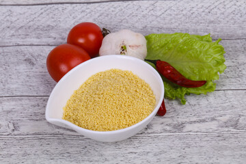 Raw couscous in the bowl served salad leaves, tomato and pepper