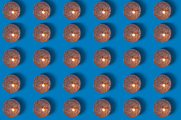Pattern. On a blue background, there are round burning candles in a row. Top view of burning shiny holiday candles. Christmas and New Year celebration concept.