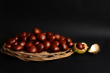 Still life horse chestnuts lie on a wicker basket on a black background