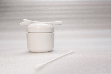 Close-up of cotton swabs with white background with white plastic jar

