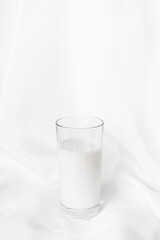 glass of milk on white fabric background, vertical orientation