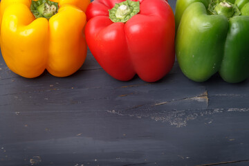 
Three raw peppers -Red, green and yellow- positioned on top on a dark gray wooden background. Photograph with space to add text.