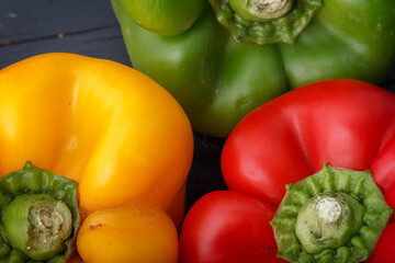 Three raw peppers.
Detail photograph of three peppers -Red, green and yellow- positioned in a circle on a dark wooden background.