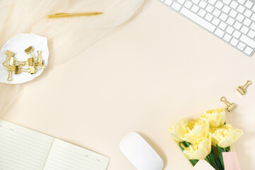 Modern home office Desk, work space with copy space, a bouquet of yellow tulips on a beige background. Lay Flat, the top view layout. Background for a freelancer woman or blogger