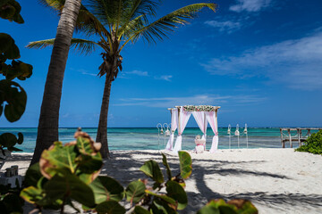 Wedding bamboo gazebo, decorated with tropical flowers and coloured fabrics on the paradise beach with palm trees, white sand and blue water of Caribbean Sea, Punta Cana, Dominican Republic 