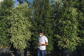 Young Caucasian male walking near green plantations with a medical mask - new normal after Covid-19