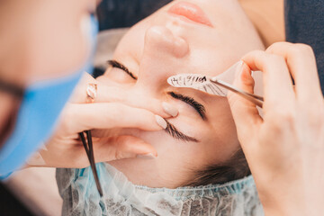 Gluing a bunch of artificial eyelashes on a girl eyelid - eyelash extension procedure woman