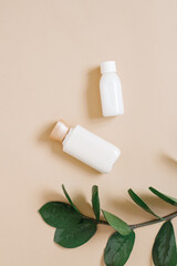 The concept of plant-based, organic cosmetics. Bottles with body or face cream and a branch of a tropical plant on a beige background.