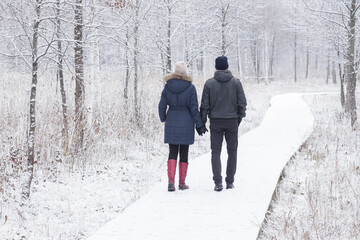 Young adult couple holding each other hands and walking on white snowy boardwalk. Peaceful...