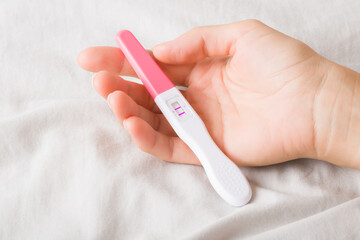 Pregnancy test with two stripes in young woman palm on bed sheet. Positive result. Closeup.