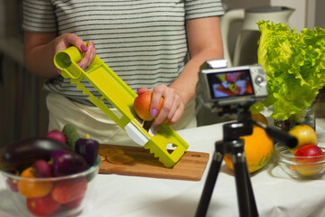 young girl cuts vegetables and shoots video for blog in the kitchen with shallow depth of field