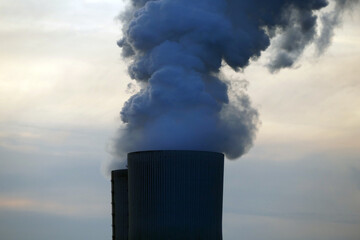 Smoke rising from a cooling tower of a power station, red-orange evening sky, concept of...