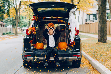 Trick or trunk. Child boy celebrating Halloween in trunk of car. Kid with red carved pumpkin...