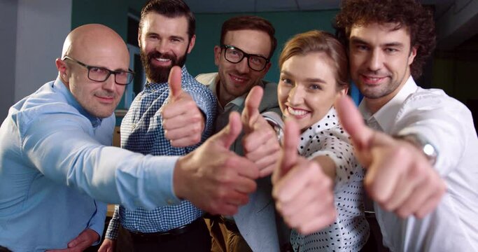 Portrait of happy adult european office workers thumb up. Successful business people smiling and posing for camera.