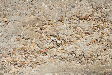 Gravel and cement ground with small stones protruding from the wall. Textured background.