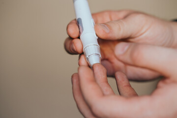 Medicine, diabetes, glycemia, healthcare and people concept - close up of a man's hands using a lancet on his finger to check blood glucose meter with copy space for text