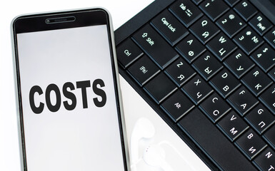 The word COST is written on the phone that is on the laptop keyboard. Financial concept