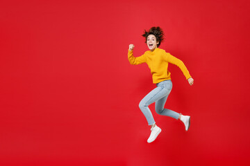 Fototapeta na wymiar Full length side view excited surprised laughing beautiful young brunette woman 20s wearing basic casual yellow sweater jumping like running isolated on bright red colour background studio portrait.