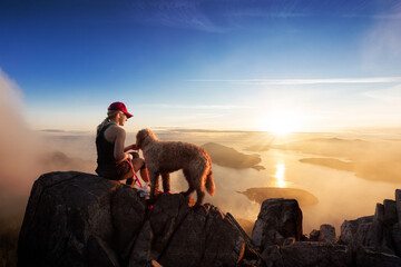 Adventurous Girl is hiking with a dog on top of St. Mark's Mountain during a sunny summer sunset. Located in West Vancouver, British Columbia, Canada. Concept: Adventure, Lifestyle, Friendship