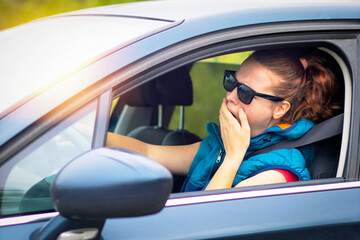 A woman drives a car, a woman in a traffic jam in sunglasses, yawns covering her mouth. Fall asleep...