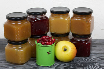 Jam in jars. There is an apple and cranberry nearby. On black pine boards.