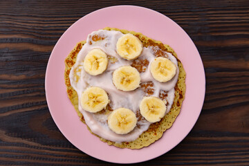 pancakes with yogurt lie on a plate with banana rings on a wooden background