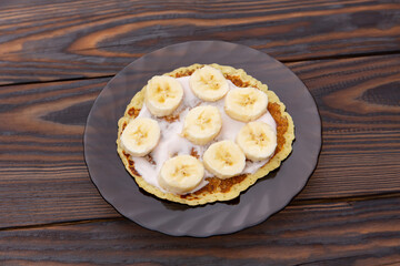 pancakes with yogurt lie on a plate with banana rings on a wooden background