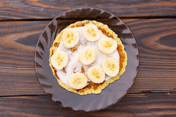 pancakes with yogurt lie on a plate with banana rings on a wooden background