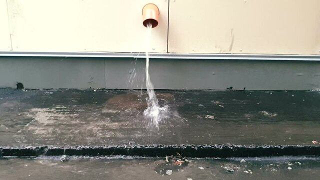 Waste water discharge system in a modern building. Downpipe from which a stream of water pours in heavy rain. Storm water drainage
