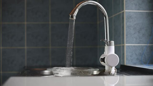 Mans hand opens the faucet in kitchen sink, water leaking from the tap