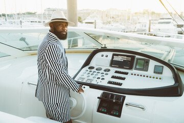 A handsome wealthy mature bearded black guy in a hat and a striped summer costume with shorts is...