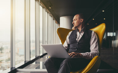 A confident relaxed successful mature man entrepreneur sitting with a laptop on an orange armchair...