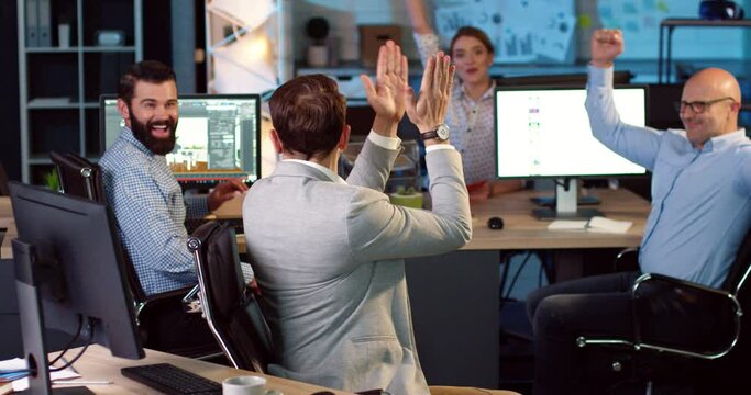 Adult office worker in jacket looking at computer screen and receives good news. Happy man reacting emotionally and shares joy of success with colleagues.