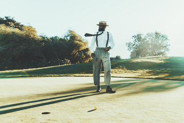 A fashionable mature bearded black guy in a hat, white shirt, and trousers with suspenders is...