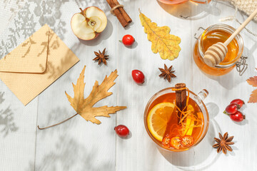 Autumn flatlay with hot tea, a jar of honey, dry leaves and rosehip berries. On a light background with shadows.