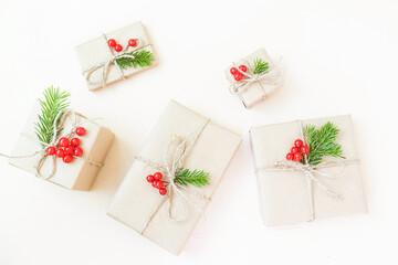 Christmas eco flat lay: gifts wrapped in craft paper, spruce branches and red berries as a decoration. Sustainability concept.