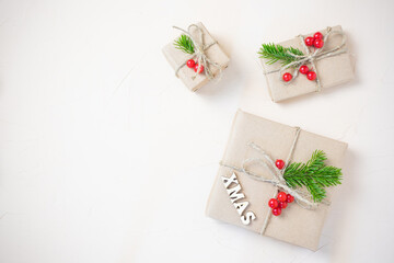 Christmas eco flat lay: gifts wrapped in craft paper, spruce branches and red berries as a decoration. Sustainability concept.
