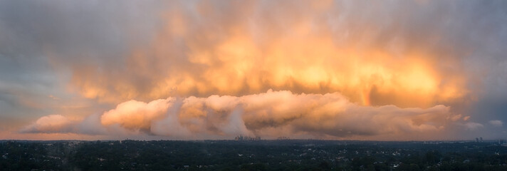 Panorama of storm front over Sydney CBD Australia lit by the setting sun creating orange and yellow...