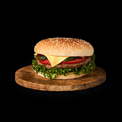 Delicious classic burger on wooden cutting board isolated on black background