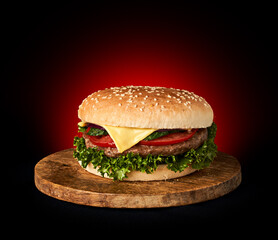 Delicious classic burger on wooden cutting board isolated on black background