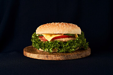 Delicious classic burger on wooden cutting board isolated on black background