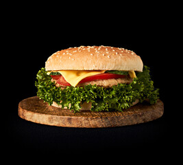 Delicious classic burger on wooden cutting board isolated on black background