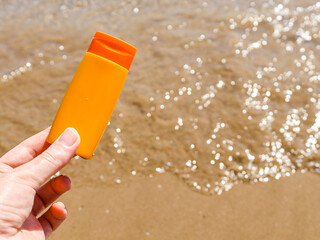 sunscreen on the beach
Hand holds sunscreen on the left with sea view and with space for text on the right, close-up side view.