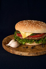 Delicious classic burger on wooden cutting board isolated on black background