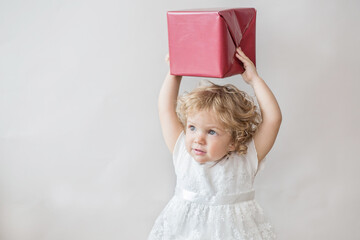 Happy curly girl in white dress with Christmas gift on light gray background 