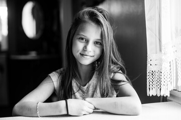 Cute ten-year-old girl posing for the camera sitting at the table. Black and white photography.