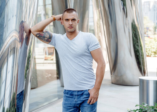 A young man leans on a shiny column. Courageous guy with a firefighter tattoo on his biceps. Male portrait.
